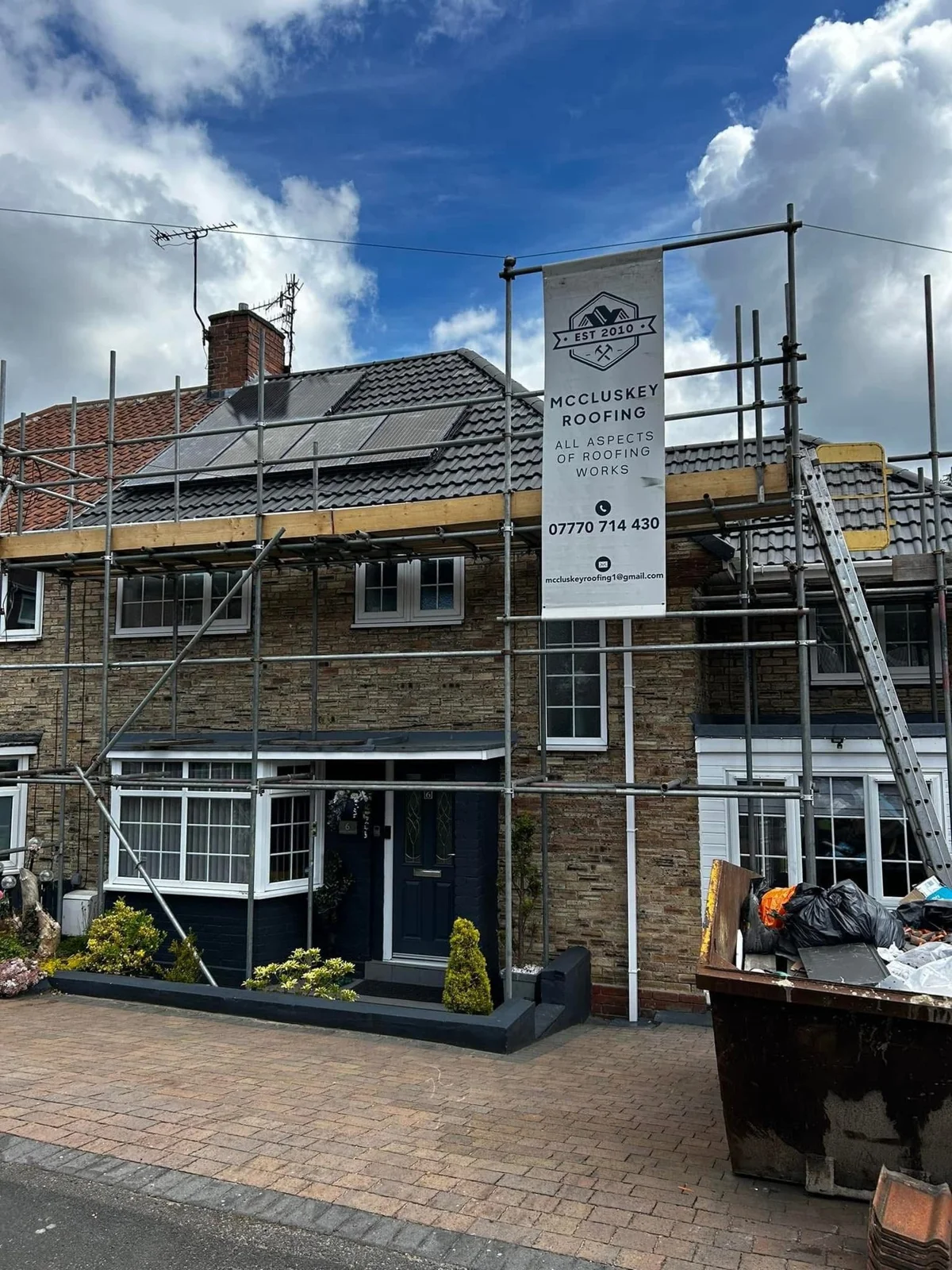 House under scaffolding with a McCluskey Roofing company sign