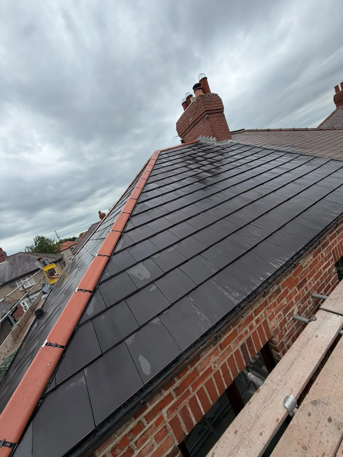 Dark slate roof with terracotta hip tiles and a brick chimney