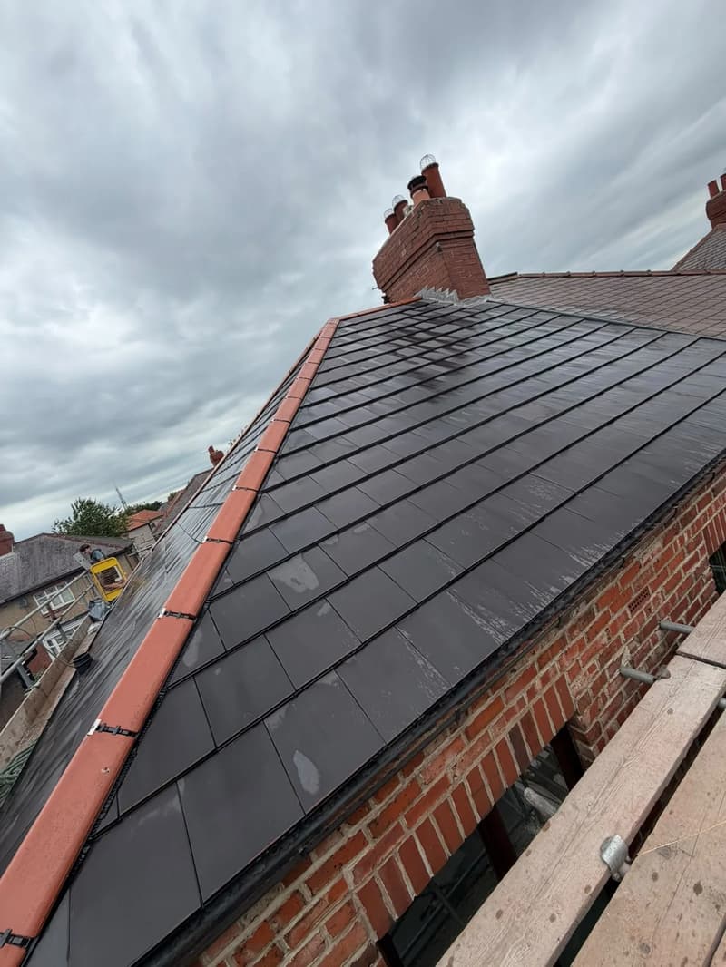 Dark slate roof with terracotta hip tiles and a brick chimney