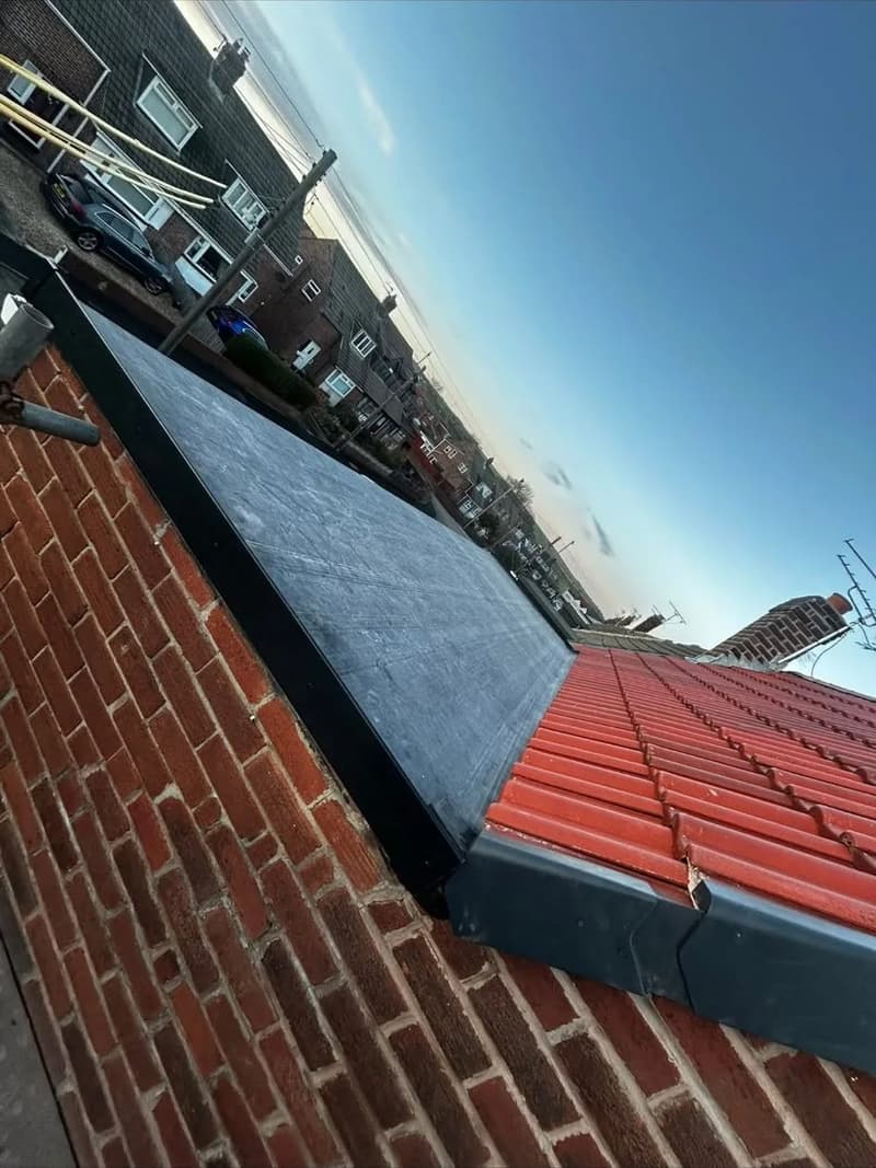 EPDM flat roof beside red roof tiles with dry verge trim