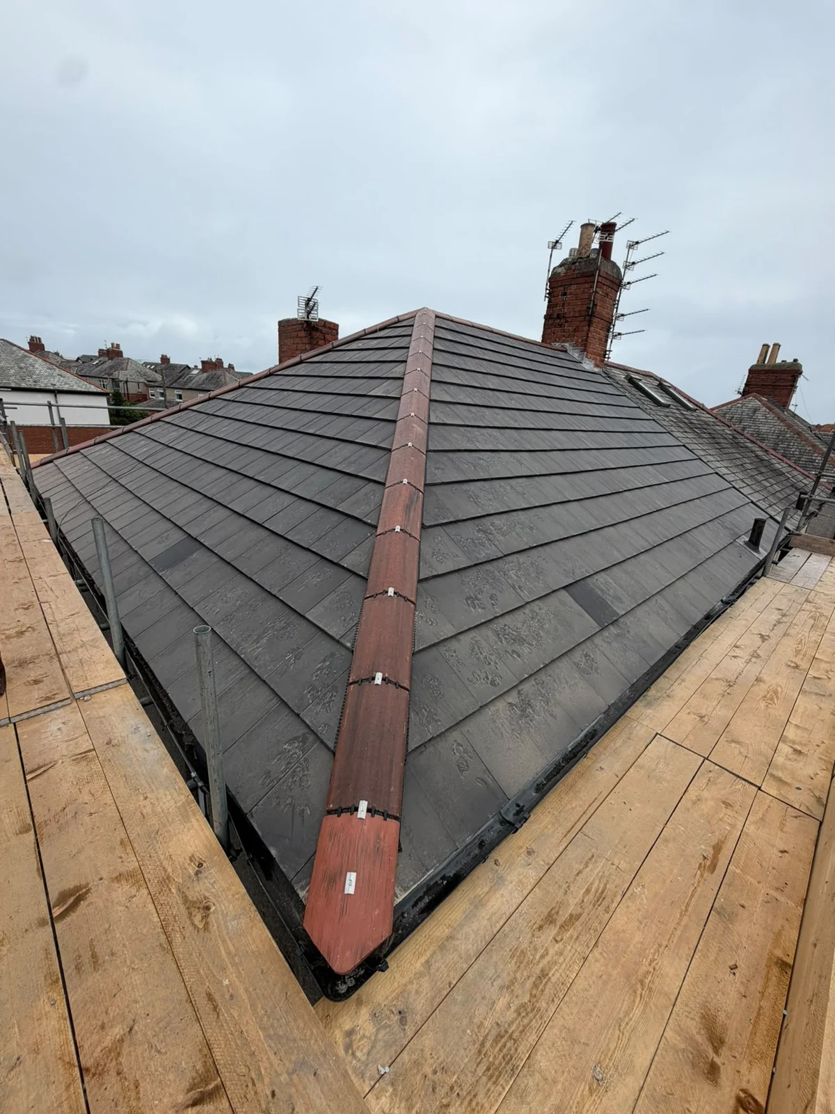 New grey tiled hip roof with red hip tiles and scaffolding