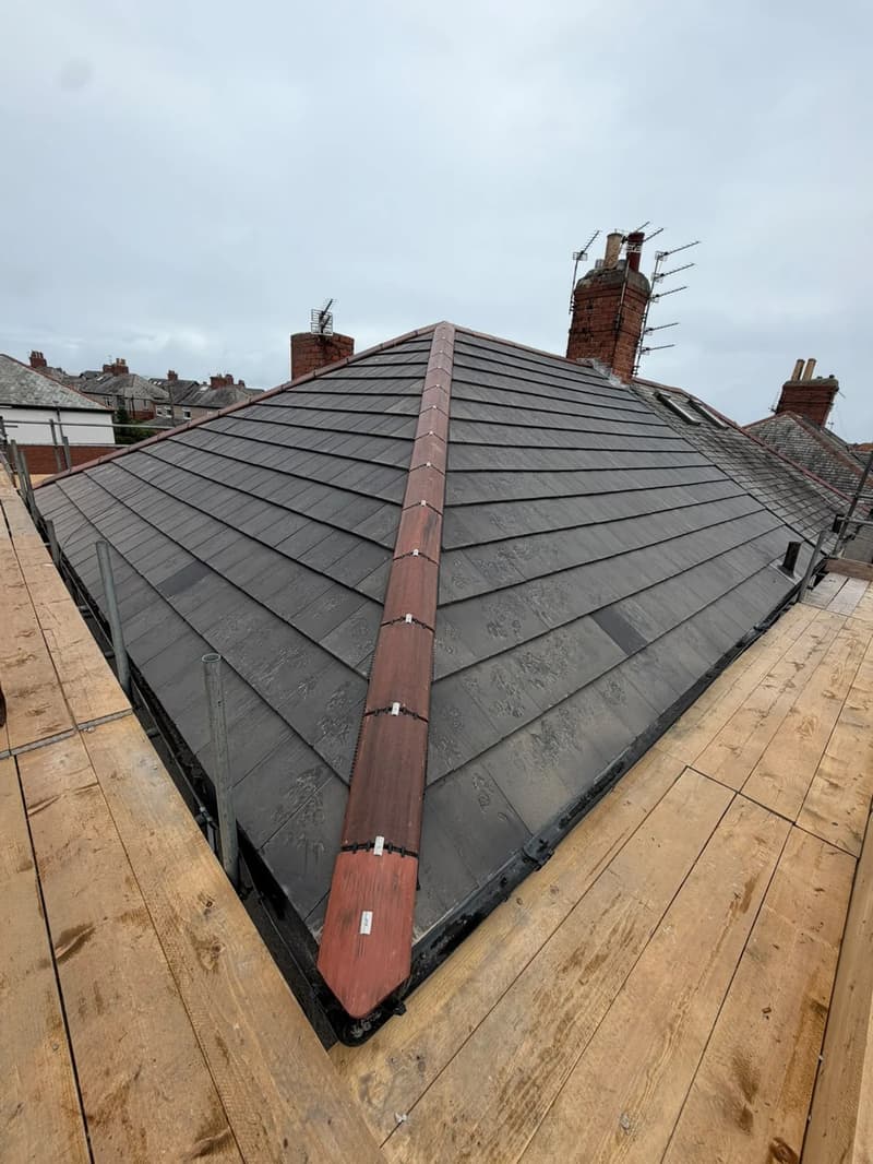 New grey tiled hip roof with red hip tiles and scaffolding